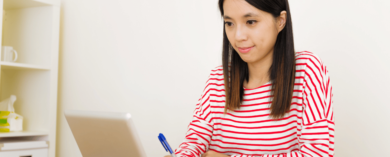 asian woman writing in front of laptop